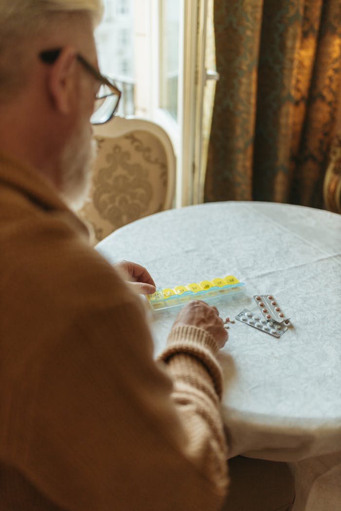 Elderly man sorting pills at a table, focusing on health and wellness.